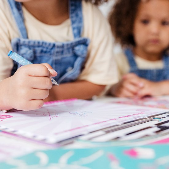 Enfant dessinant avec un stylo bleu dans un livre d'activités Gabby's Dollhouse.