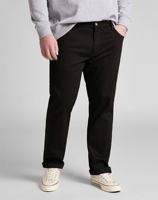 Man in een grijze sweater en zwarte jeans, met opgerolde broekspijpen. Draagt crèmekleurige sneakers.
