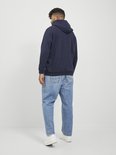 Man in een donkerblauwe hoodie, kijkend weg. Hij draagt een jeans.