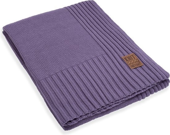 Een opgevouwen wollen plaid in de kleur violet, met een gebreid patroon en een bruin label.