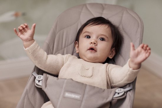 Baby in zandgrijs wipstoeltje met beige gebreide trui.