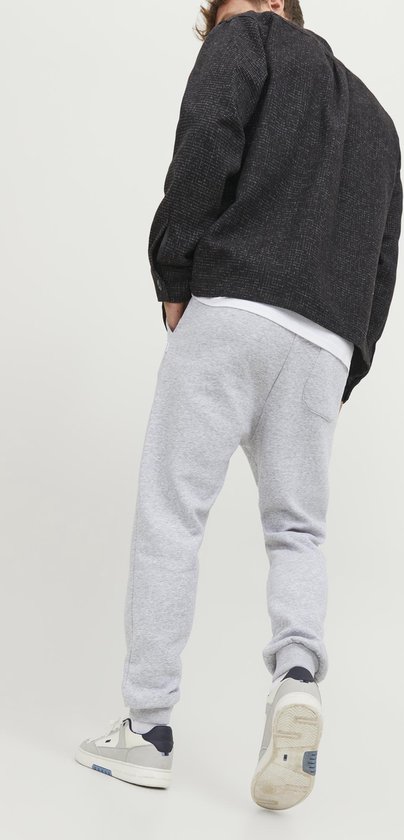 Man van achteren gezien, met lichtgrijze joggingbroek, wit T-shirt en zwart jasje.