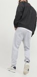 Man van achteren gezien, met lichtgrijze joggingbroek, wit T-shirt en zwart jasje.