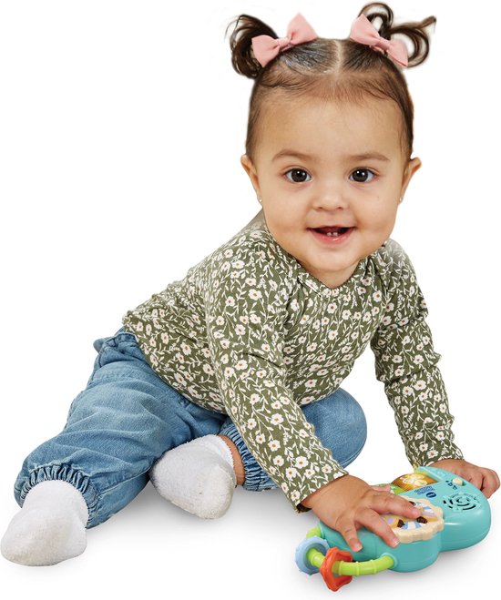 Baby met de VTech Tummy Time Knuffelhertje piano. Zittend op een kleed met jeans en witte sokken.