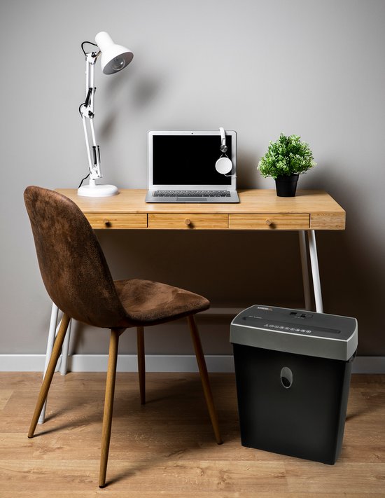 Zwarte papierversnipperaar naast een bureau met laptop en stoel.