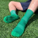 Homme assis sur l'herbe, portant des chaussettes vertes avec crampons et un short sombre.