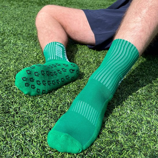 Homme assis sur l'herbe, portant des chaussettes vertes avec crampons et un short sombre.