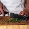 Een chef-kok snijdt bieslook met een Japans mes met damastpatroon en zwart handvat.
