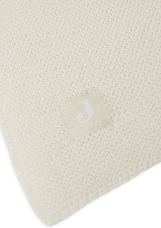 Gros plan d'une couverture en maille crème avec une étiquette Jollein.