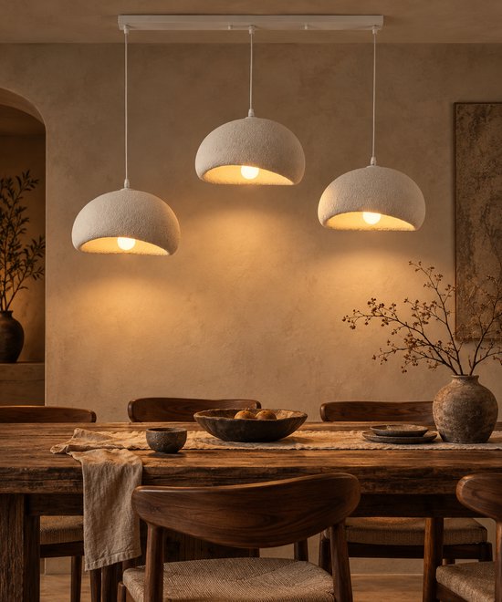 Drie witte, halfronde hanglampen met een ruw textuur boven een houten eettafel met stoelen.
