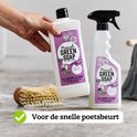 Hand met Marcel's Green Soap allesreiniger spray met lavendel en rozemarijn, naast een borstel.