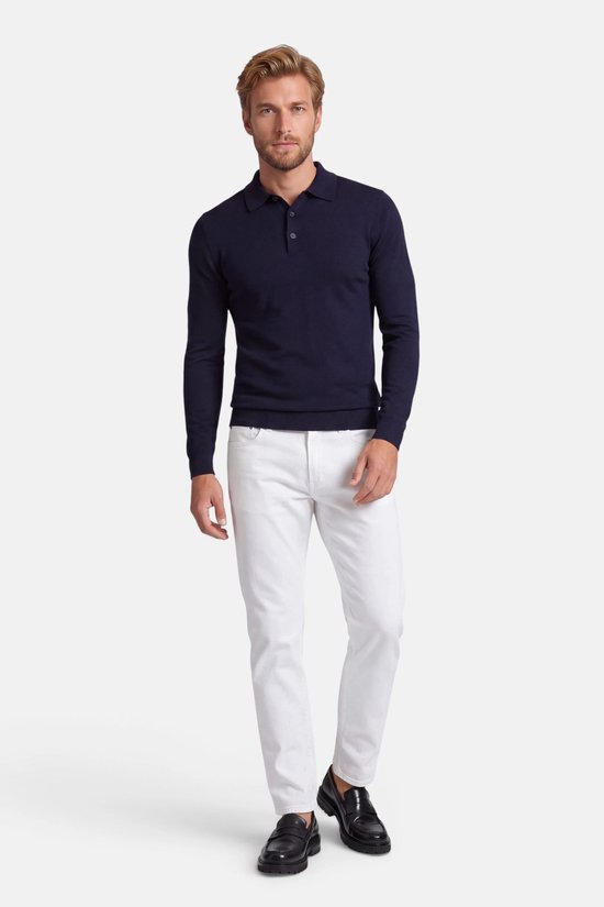 Model draagt een marineblauwe polo met lange mouwen, witte broek en zwarte loafers.