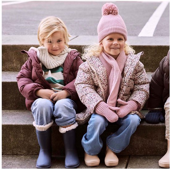 Jongen in bruine jas naast een meisje met roze muts en sjaal, zittend op een trap.