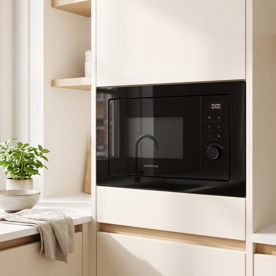 Zwarte Inventum magnetron met grill in een witte keuken, naast een plant en een vaas.