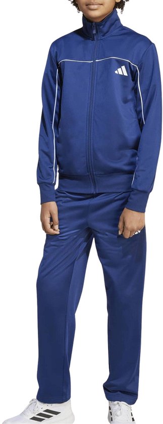 Jongens die een marineblauw Adidas trainingspak dragen met witte biezen. De jongen kijkt naar de camera.