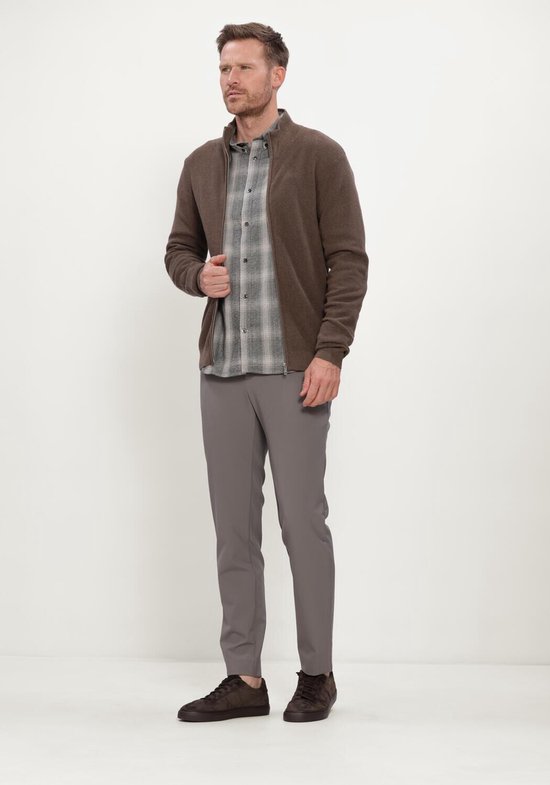 Man in grijze chino broek, grijs ruitjes overhemd en bruine vest, staand.