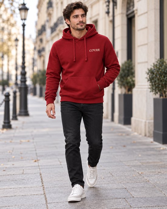 Man met donkere jeans, witte sneakers en rode COVAR hoodie met capuchon, lopend.