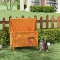 Oranje houten kattenhuis voor buiten met een openklapbaar dak, in een tuin met een hek.