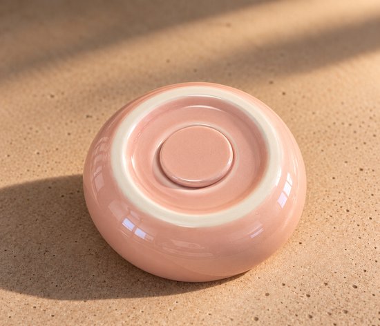 Onderkant van de ronde, roze keramische urn met witte basisring.