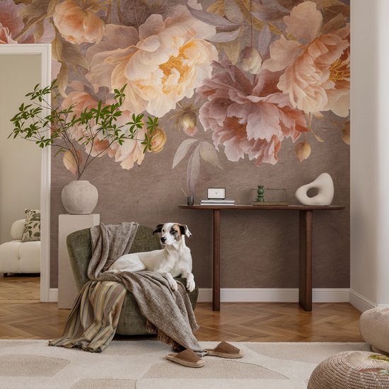 Wand met bruin behang en grote bloemen in zachte tinten. Een hond ligt op een groene fauteuil met een plaid.