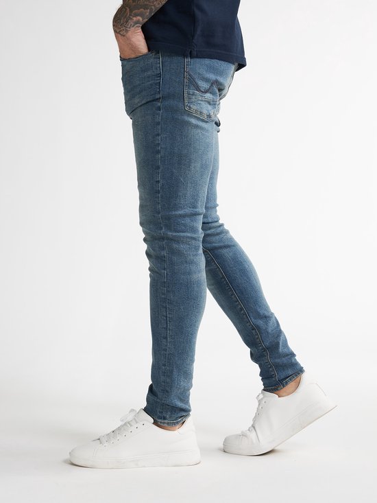 Man in een donkerblauwe skinny jeans met lichte wassing en witte sneakers.