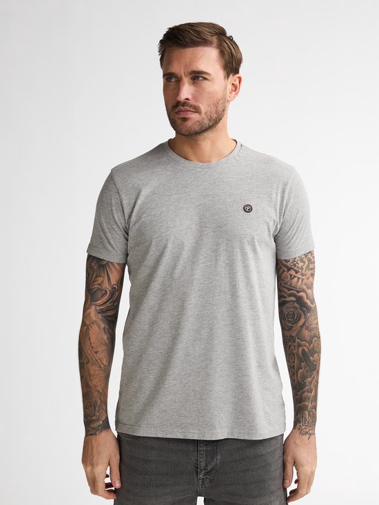 Model met tatoeages draagt een grijs t-shirt met het Petrol Industries logo, gecombineerd met een donkergrijze jeans.