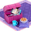 Roze kist met accessoires voor poppen: een modeboek, schaar, stof, kussens, kopje en gebakjes.