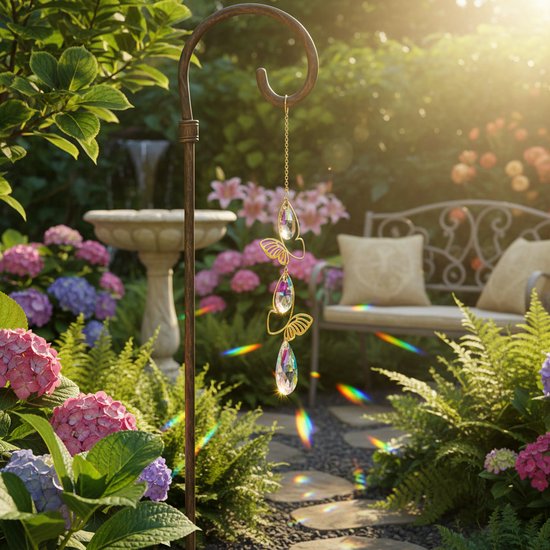 Gouden hanger met vlinders en druppelvormige kristallen, in een tuin met bloemen en een bankje.