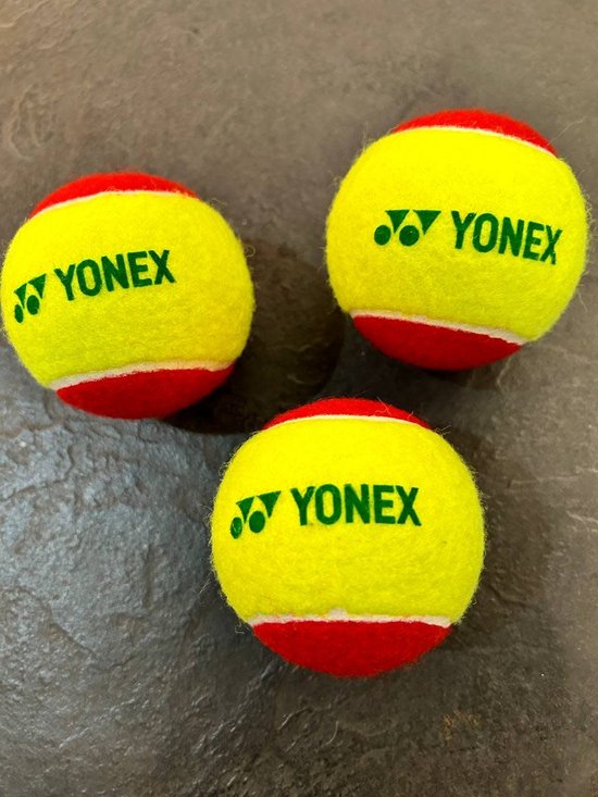 Drie Yonex tennisballen, geel met rode rand en "YONEX" logo, liggend op een donkere ondergrond.