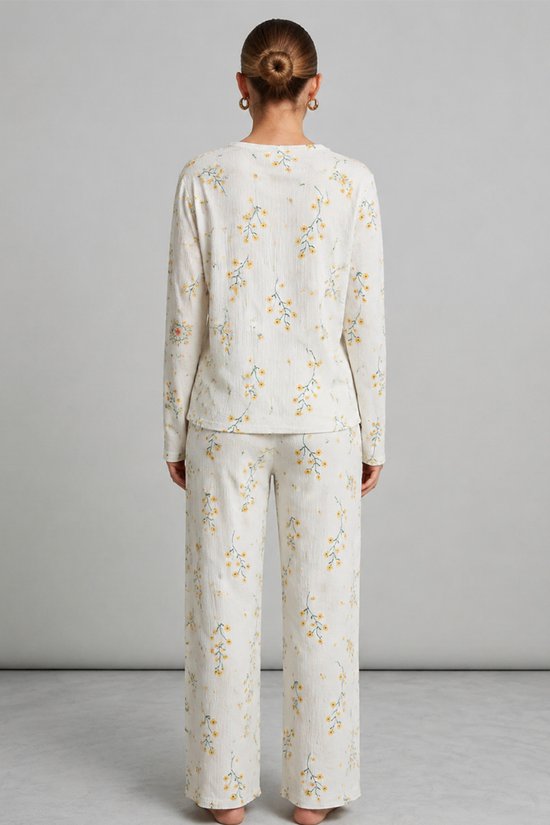 Achteraanzicht van de ecru pyjamaset met gele bloemenprint en een textuur in de stof.