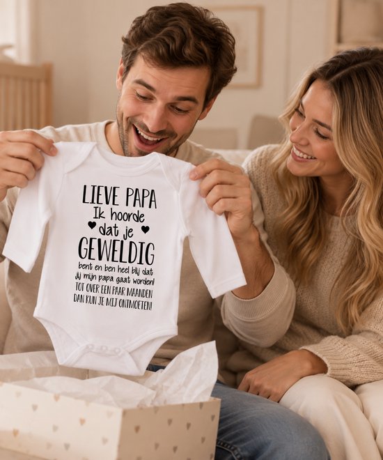 Stel die een witte babyromper vasthoudt met de tekst 'Lieve papa ik hoorde dat je geweldig bent' als zwangerschapsaankondiging.