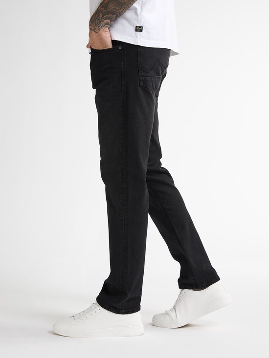Man in een zwarte straight fit jeans met omgeslagen broekspijpen, getailleerd en witte sneakers.