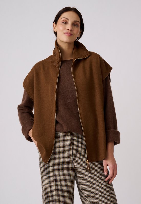 Model draagt een open bruin mouwloos vest over een donkerbruine trui en geruite broek.
