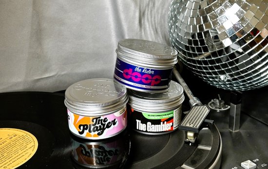 Drie potten haarstylingproducten op draaitafels en vinylplaten. Eén pot is 'the Ruler', één is 'The Player', en één is 'The Gambler'.