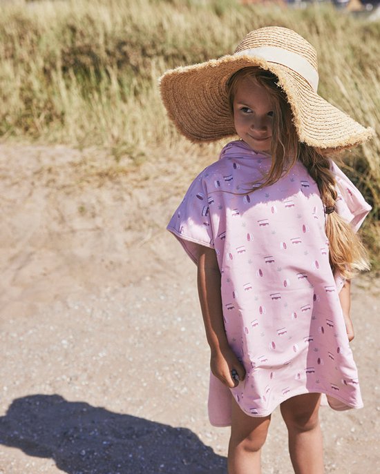 Fille portant un chapeau de paille, vêtue d'un poncho de bain rose orné de planches de surf blanches et de vagues.