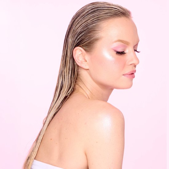 Zijaanzicht van een vrouw met nat ogend blond haar, roze oogschaduw en een glanzende teint.
