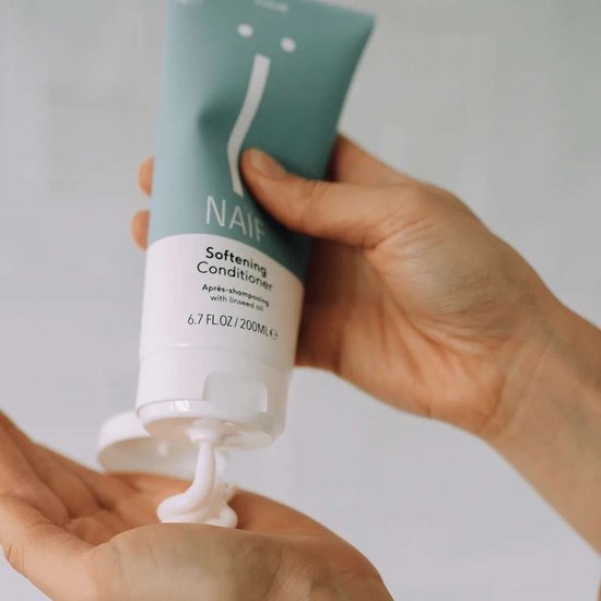 Handen die Naïf Softening Conditioner uit een lichtblauwe tube in de handpalm knijpen.