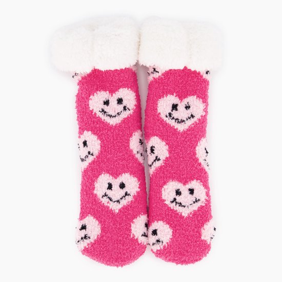 Roze, pluizige huissokken voor kinderen met wit, harig boord en een patroon van roze hartjes met lachende gezichtjes.