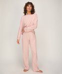 Model draagt een zachtroze pyjamaset met lange mouwen en een broek met een all-over print van kleine witte hartjes.
