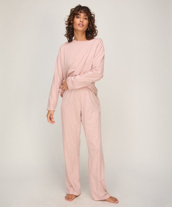 Model draagt een zachtroze pyjamaset met lange mouwen en een broek met een all-over print van kleine witte hartjes.