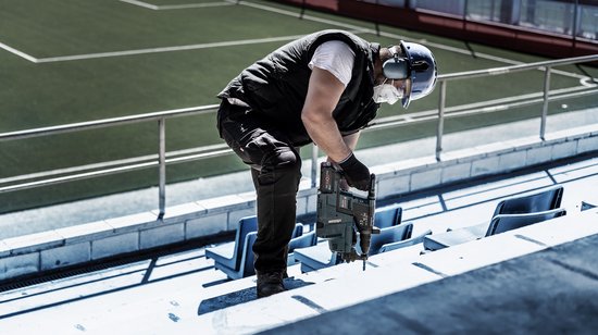 Vakman in veiligheidsuitrusting gebruikt Bosch boorhamer op een tribune van beton.