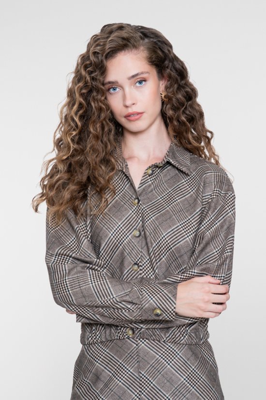 Vrouw met krullend haar draagt een bruine jas met ruitpatroon en knoopsluiting.