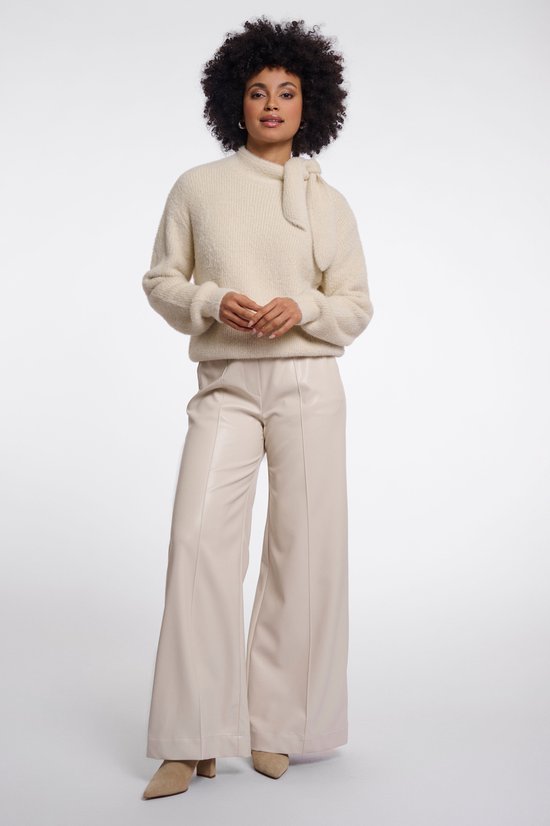 Model draagt een beige gebreide trui met opstaande kraag en knoopdetail, gecombineerd met wijde beige broek.