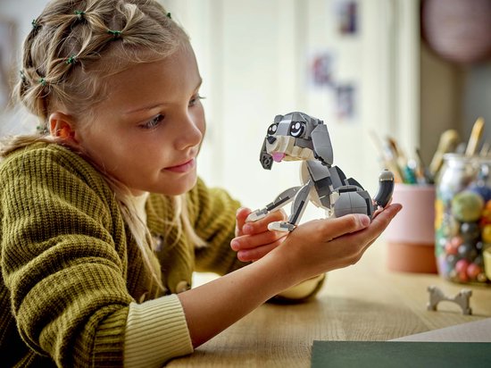Fille tenant un chien LEGO gris avec de grands yeux et un sourire joueur.