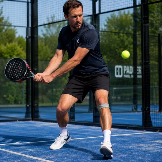 Man in donkerblauw shirt en zwarte short met kniebrace speelt padel.