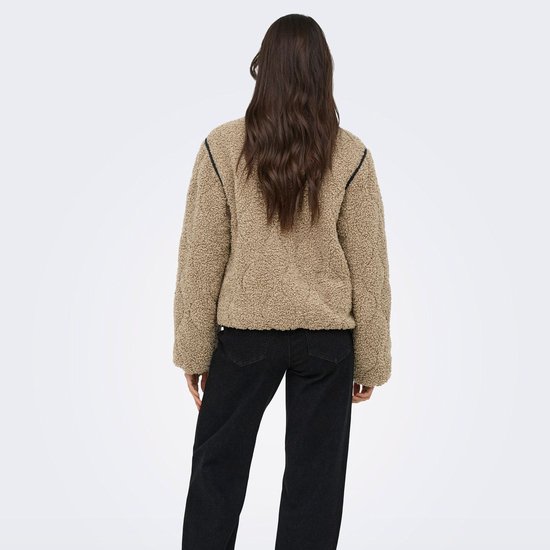 Model van achteren, draagt een beige teddy jas met zwarte bies en zwarte jeans.