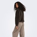 Vrouw met krullend donker haar draagt het donkerbruine faux fur jack met een bruine broek, van achteren gezien.
