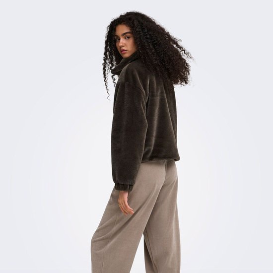 Vrouw met krullend donker haar draagt het donkerbruine faux fur jack met een bruine broek, van achteren gezien.