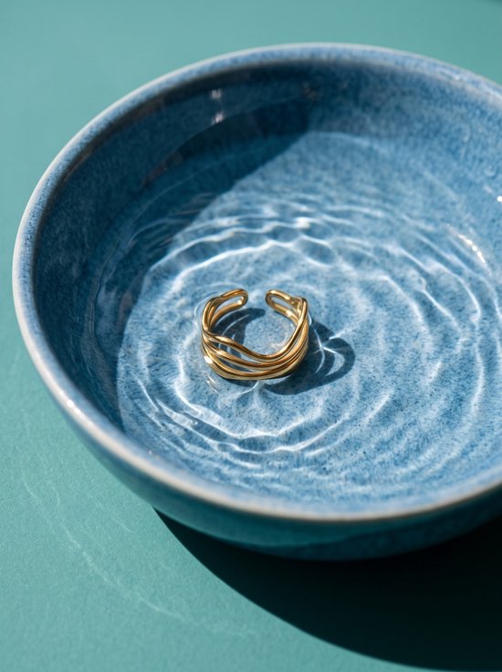 Goudkleurige, gelaagde open ring rustend in een kom met water tegen een blauwe achtergrond.