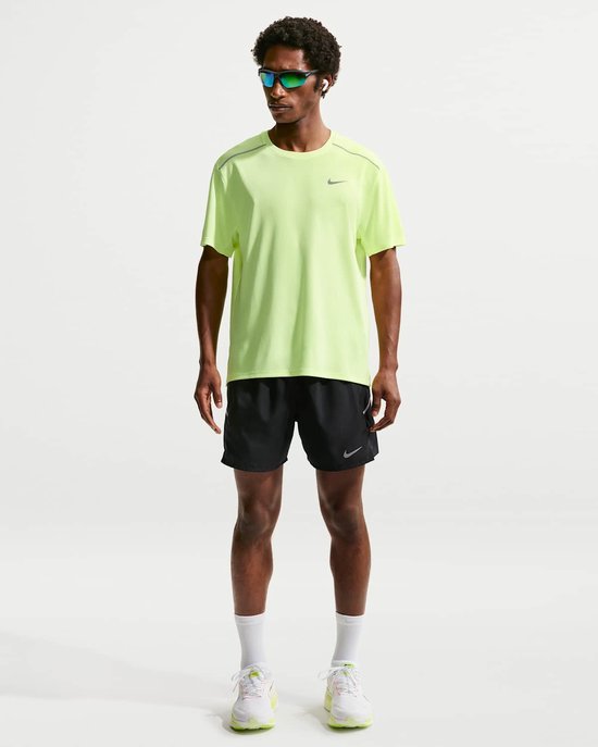 Man in felgeel Nike hardloopshirt, zwarte shorts met Nike-logo, witte sokken en sneakers.